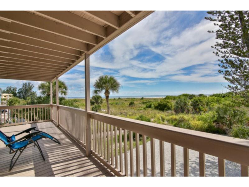A wooden deck with a blue lounge chair overlooks a coastal landscape with palm trees — 460 BEACH ROAD UNIT A1, SARASOTA, FL