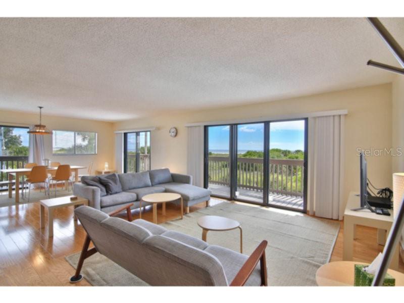 A living room with a gray sectional sofa, dining area, and sliding glass doors to a balcony — 460 BEACH ROAD UNIT A1, SARASOTA, FL