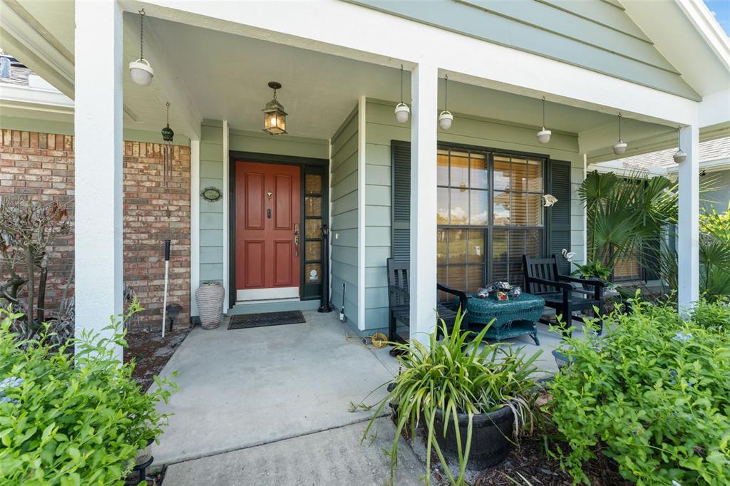 A covered front porch features a red door, light green siding, and a brick wall — 1341 S RIDGE LAKE CIRCLE, LONGWOOD, FL