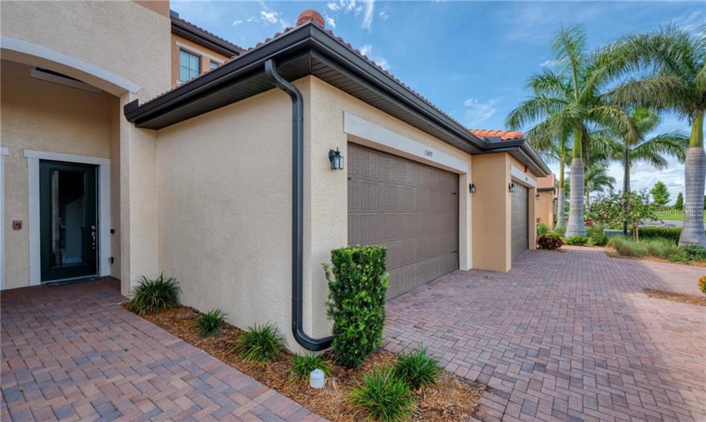 A beige stucco house exterior features a brown garage door, brick driveway, and palm trees — 23479 AWABUKI DRIVE UNIT 202, VENICE, FL