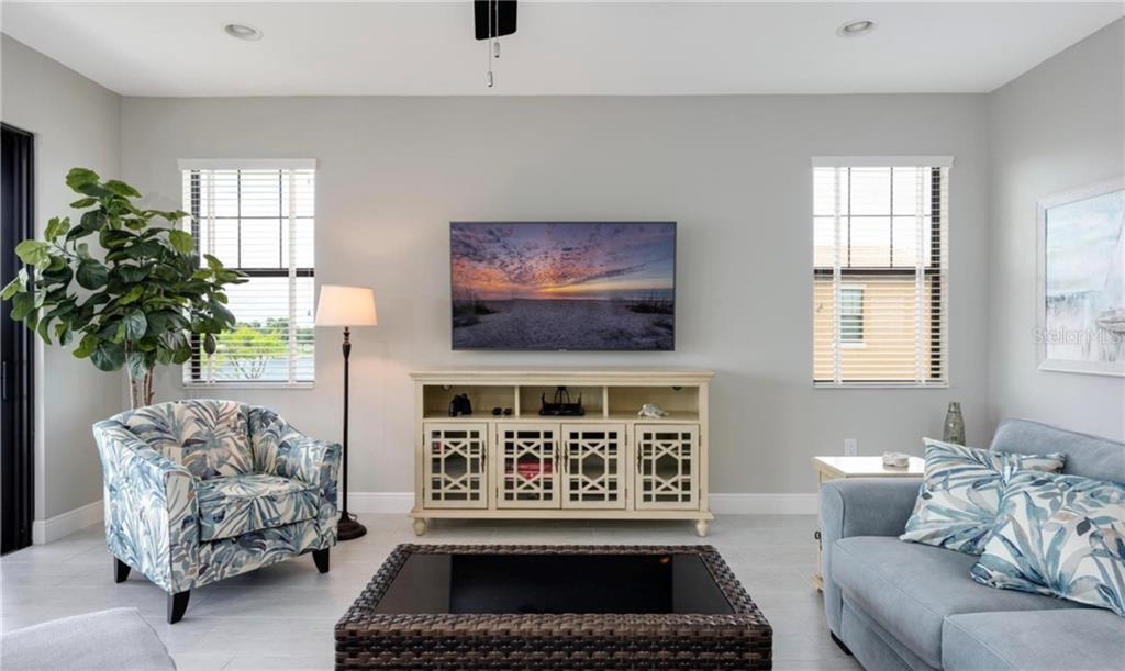 A living room features a wall-mounted television, a media console, a patterned armchair, and sofa — 23479 AWABUKI DRIVE UNIT 202, VENICE, FL