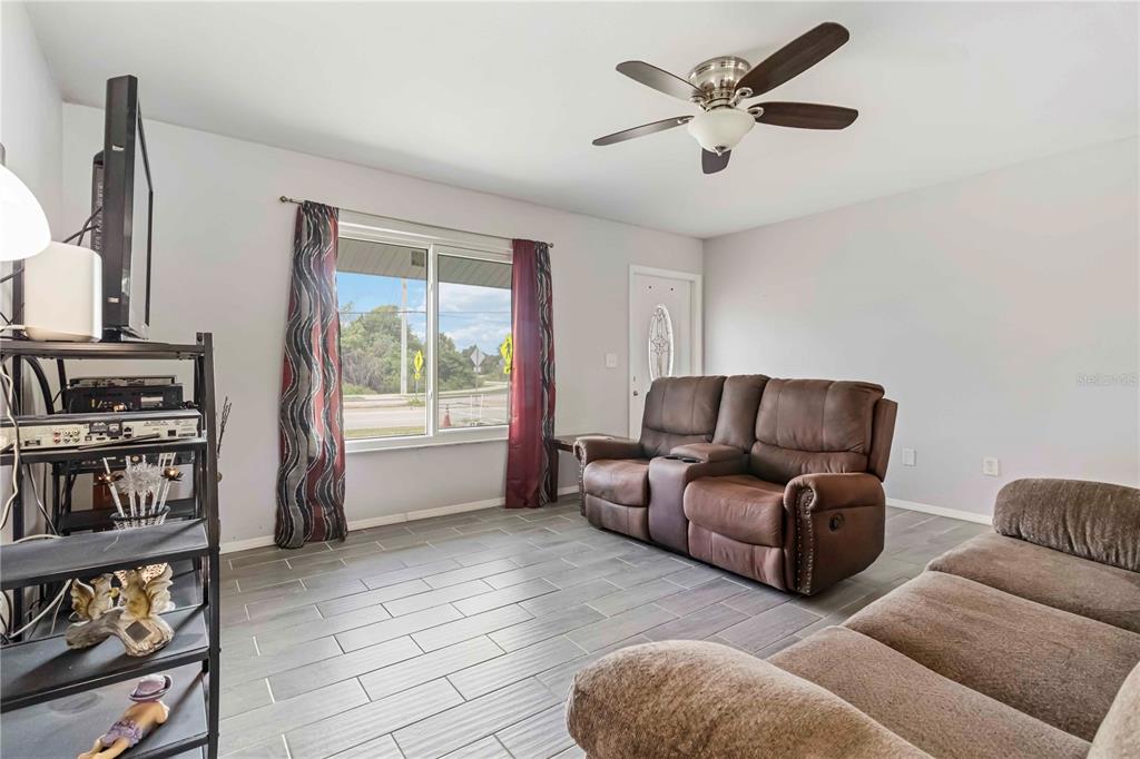 A living room features gray tile flooring, a brown leather loveseat, and a ceiling fan — 20550 EDGEWATER DRIVE, PORT CHARLOTTE, FL