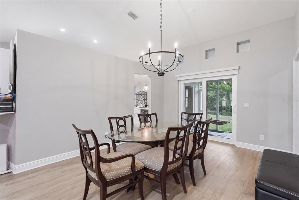 A dining room with a glass table, six chairs, a chandelier, and sliding glass doors — 9693 58TH STREET N, PINELLAS PARK, FL