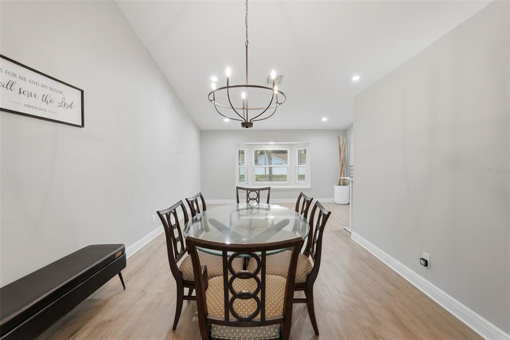 A dining room with a glass-topped table, six chairs, a chandelier, and light wood flooring — 9693 58TH STREET N, PINELLAS PARK, FL