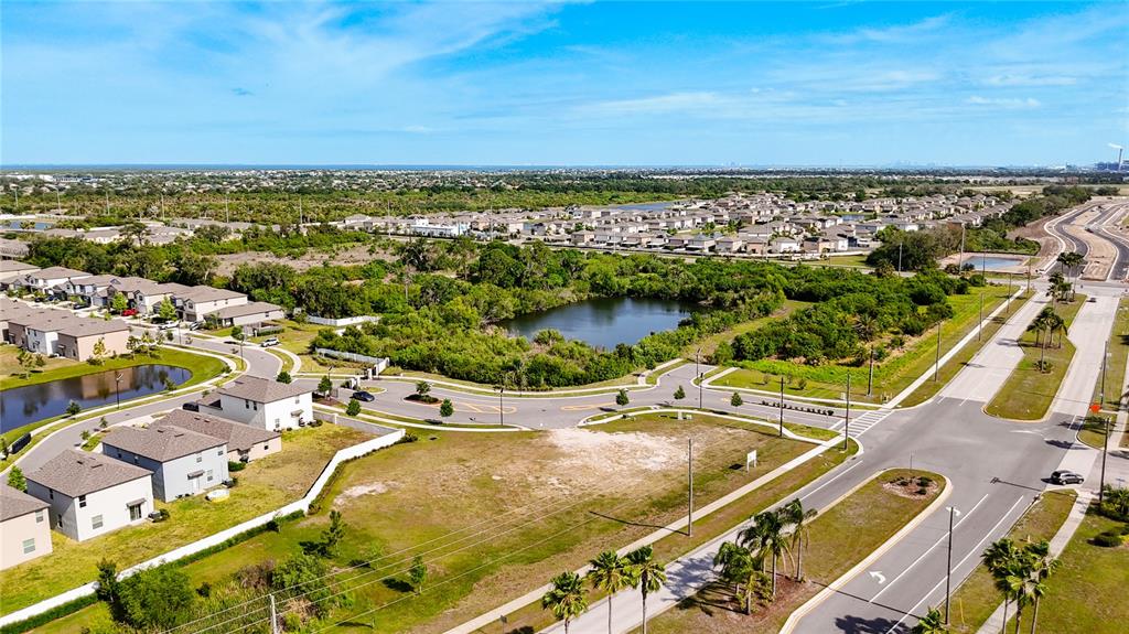 An aerial view shows a residential neighborhood with houses, a pond, and undeveloped land — 2282 JUNGLE DRIVE, RUSKIN, FL