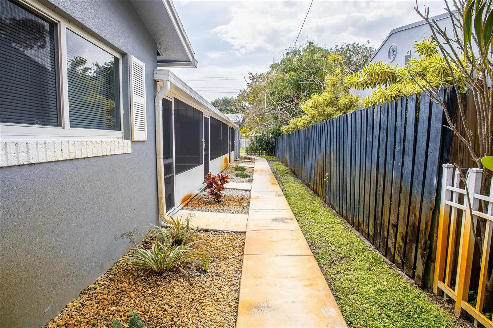 A narrow concrete walkway runs between a gray house exterior and a tall wooden fence — 2432 Sherman Street, Hollywood FL 33020, HOLLYWOOD, FL
