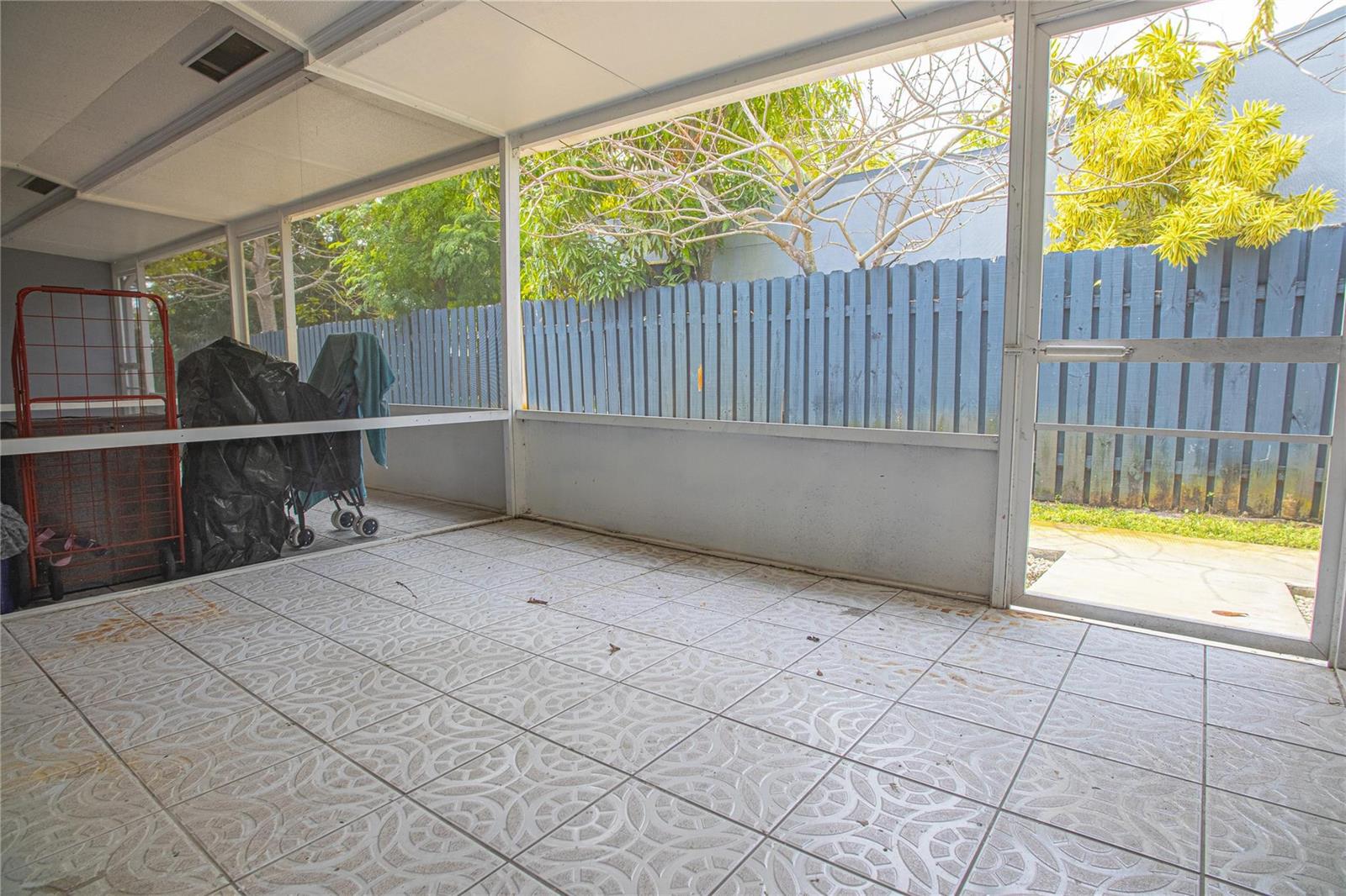 A screened-in patio features light-colored patterned tile flooring and a blue wooden fence outside — 2432 Sherman Street, Hollywood FL 33020, HOLLYWOOD, FL