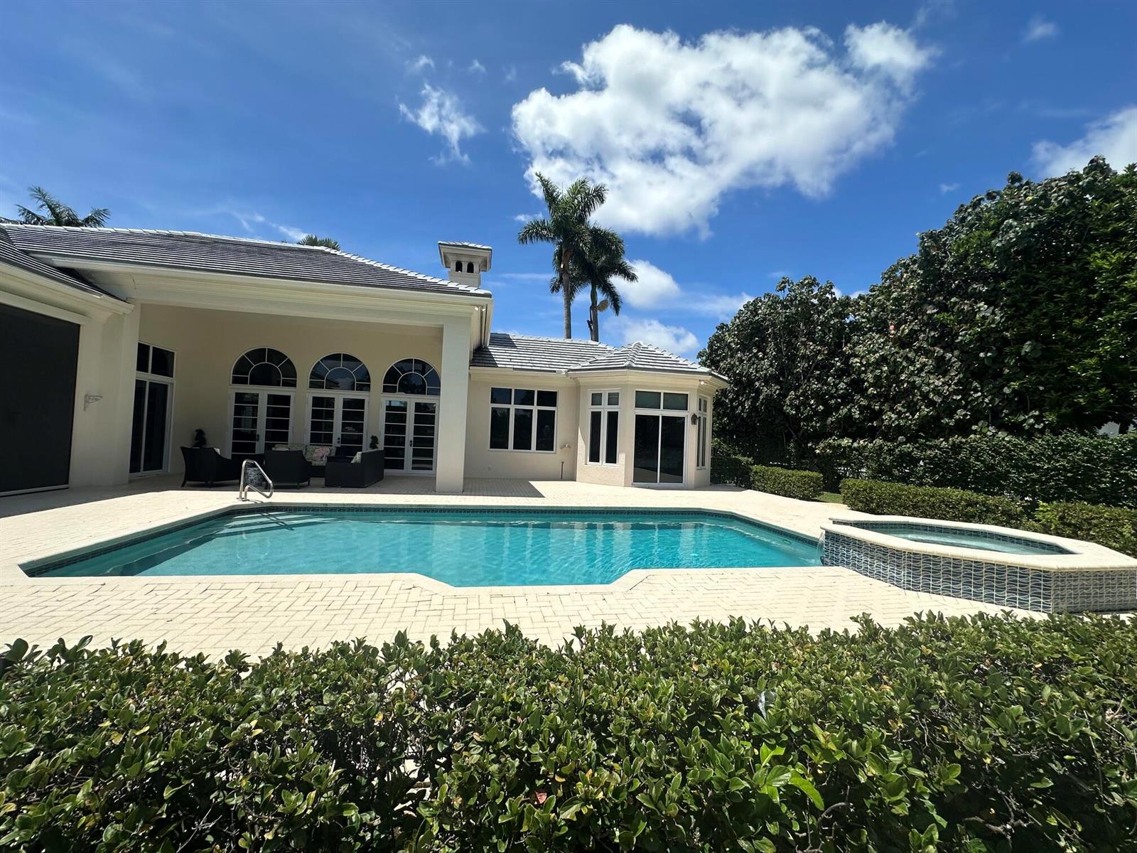A backyard features a swimming pool, a hot tub, and a patio beside a house — 645 Atlantis Estates Way, Atlantis FL 33462, ATLANTIS, FL
