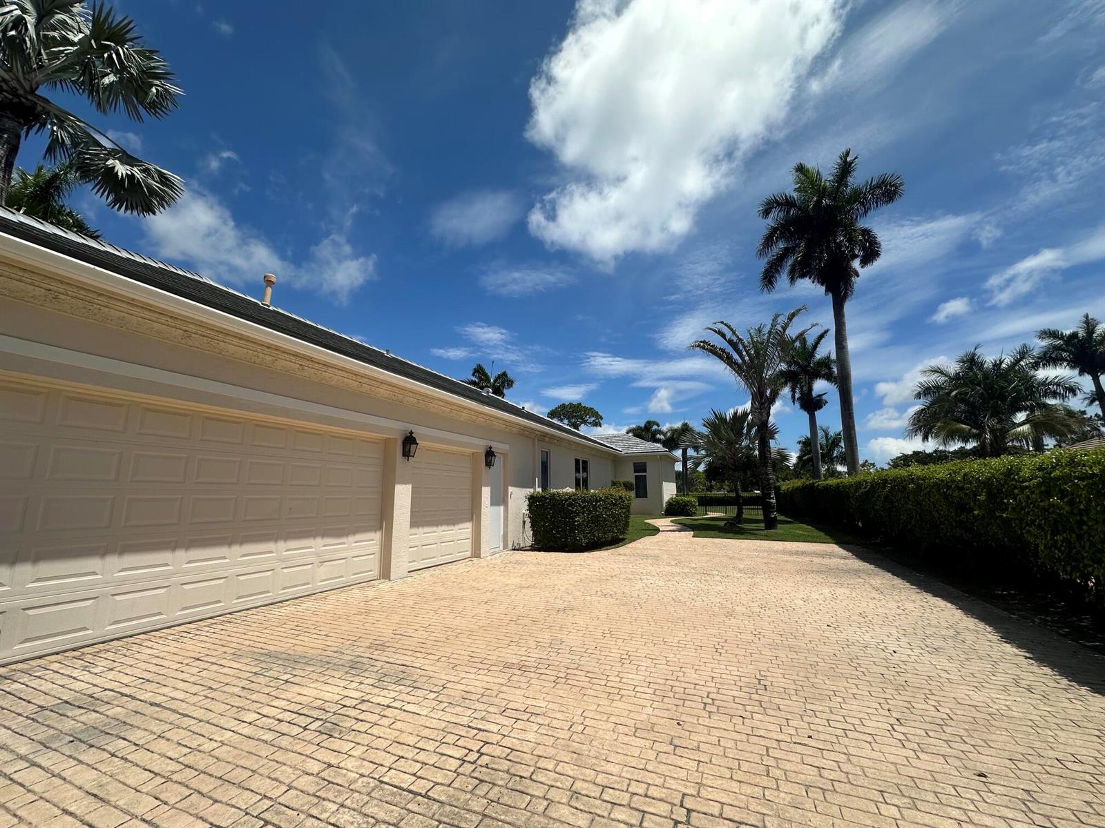 A paved driveway leads to a multi-car garage beside a house with palm trees — 645 Atlantis Estates Way, Atlantis FL 33462, ATLANTIS, FL