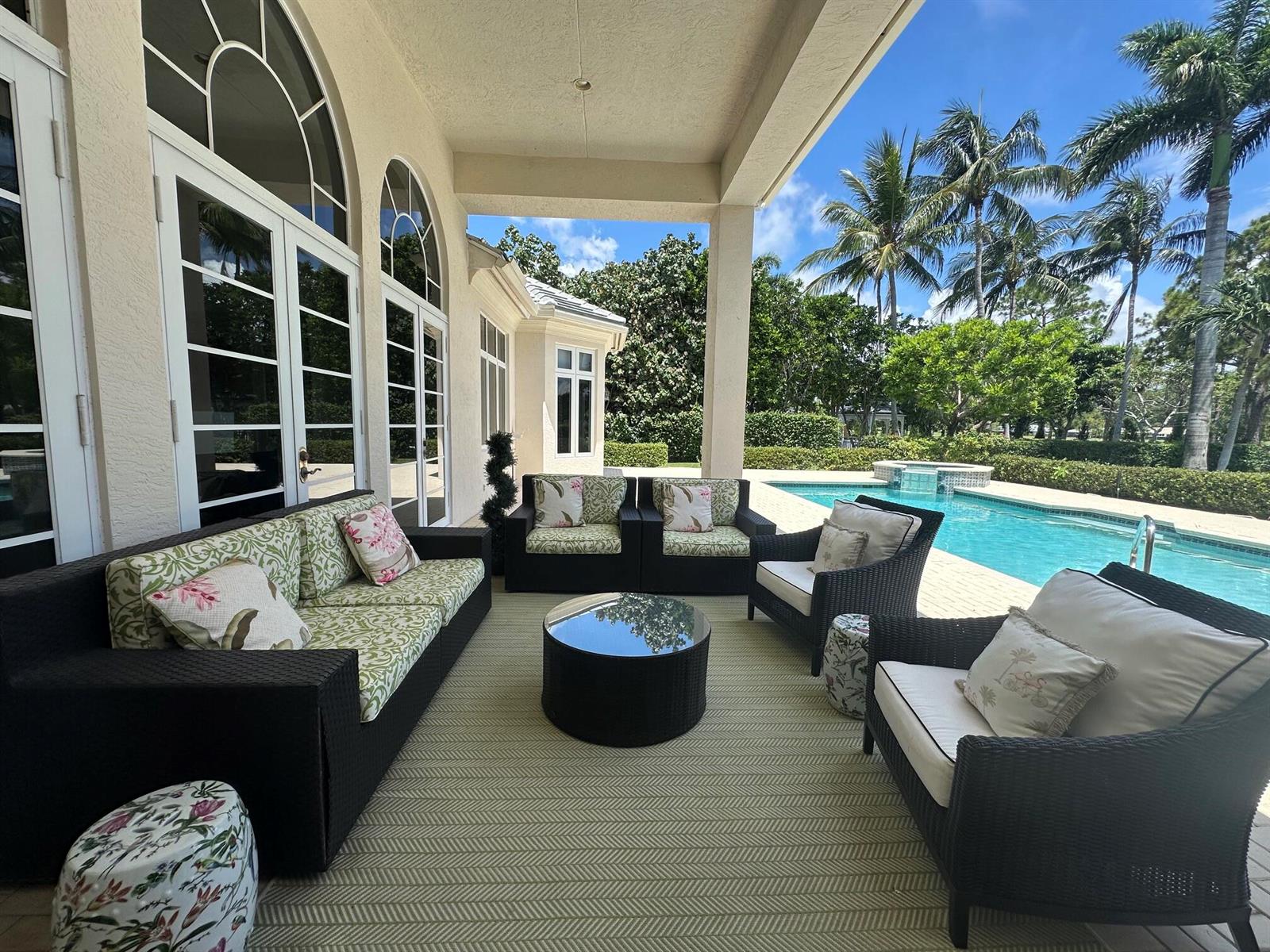 A covered patio features wicker furniture, a round coffee table, and a view of a pool — 645 Atlantis Estates Way, Atlantis FL 33462, ATLANTIS, FL