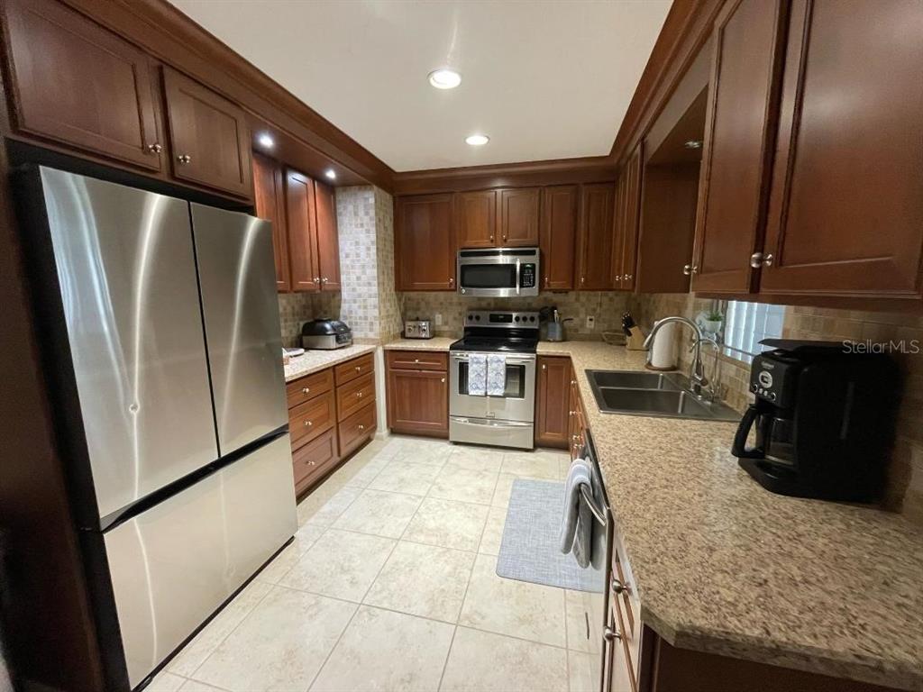 A kitchen features wood cabinets, stainless steel appliances, granite countertops, and light-colored tile flooring — 6015 CARLTON AVENUE, SARASOTA, FL