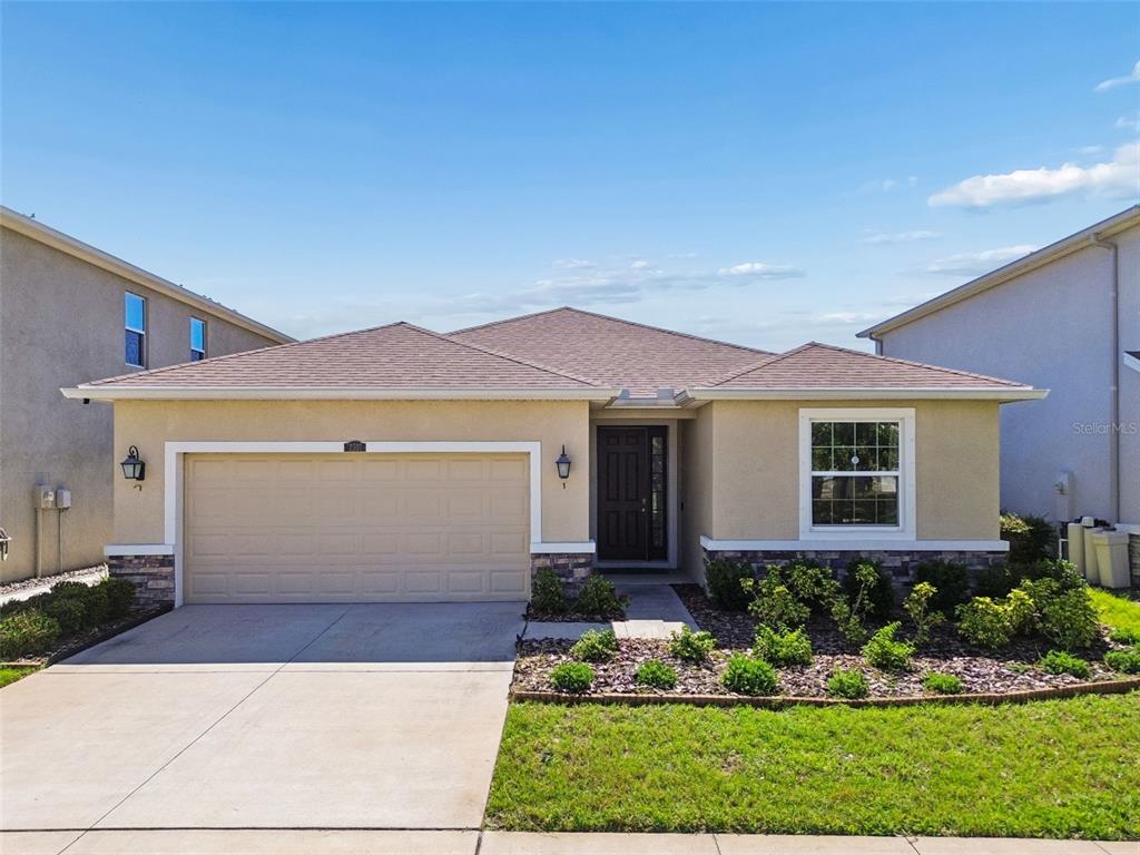 A single-story house with a tan stucco exterior, a two-car garage, and a front garden — 12507 CANDLEBERRY CIRCLE, TAMPA, FL