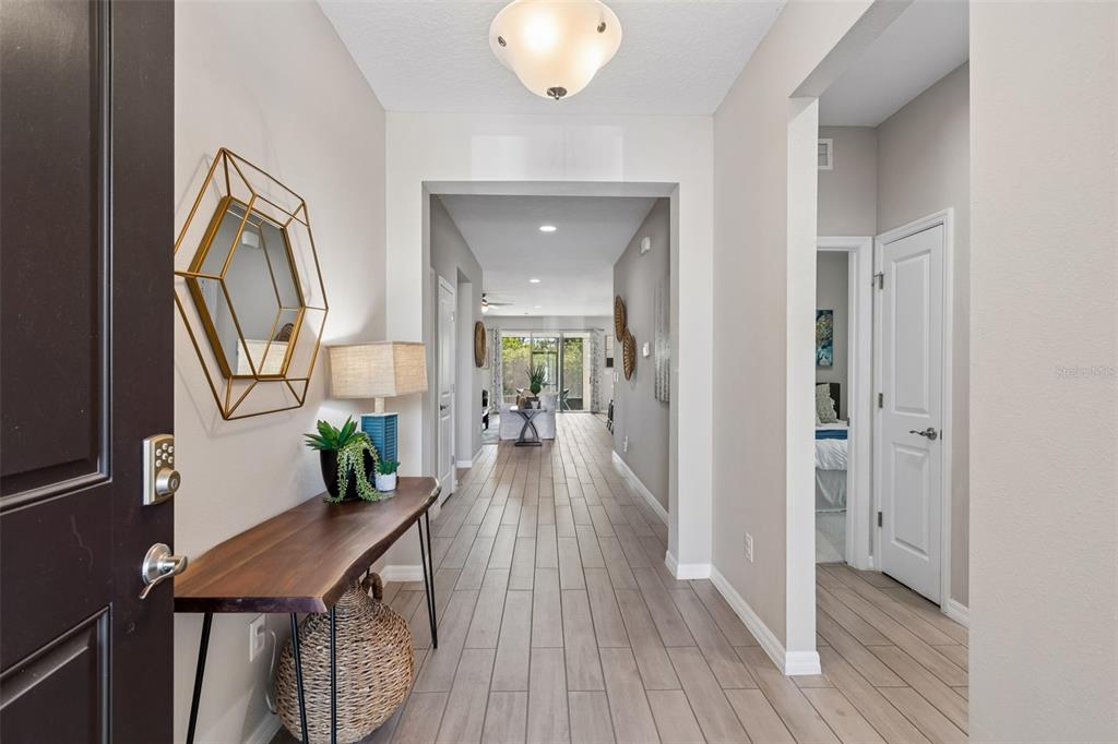 A bright entryway features a wood console table, a geometric mirror, and light wood-look flooring — 12507 CANDLEBERRY CIRCLE, TAMPA, FL
