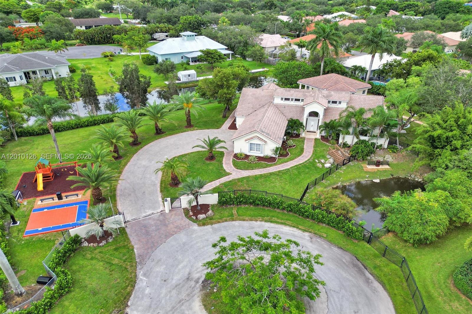 An aerial view shows a house with a circular driveway, pond, and backyard sports court — 16301 SW 62nd St, Southwest Ranches FL 33331, SOUTHWEST RANCHES, FL