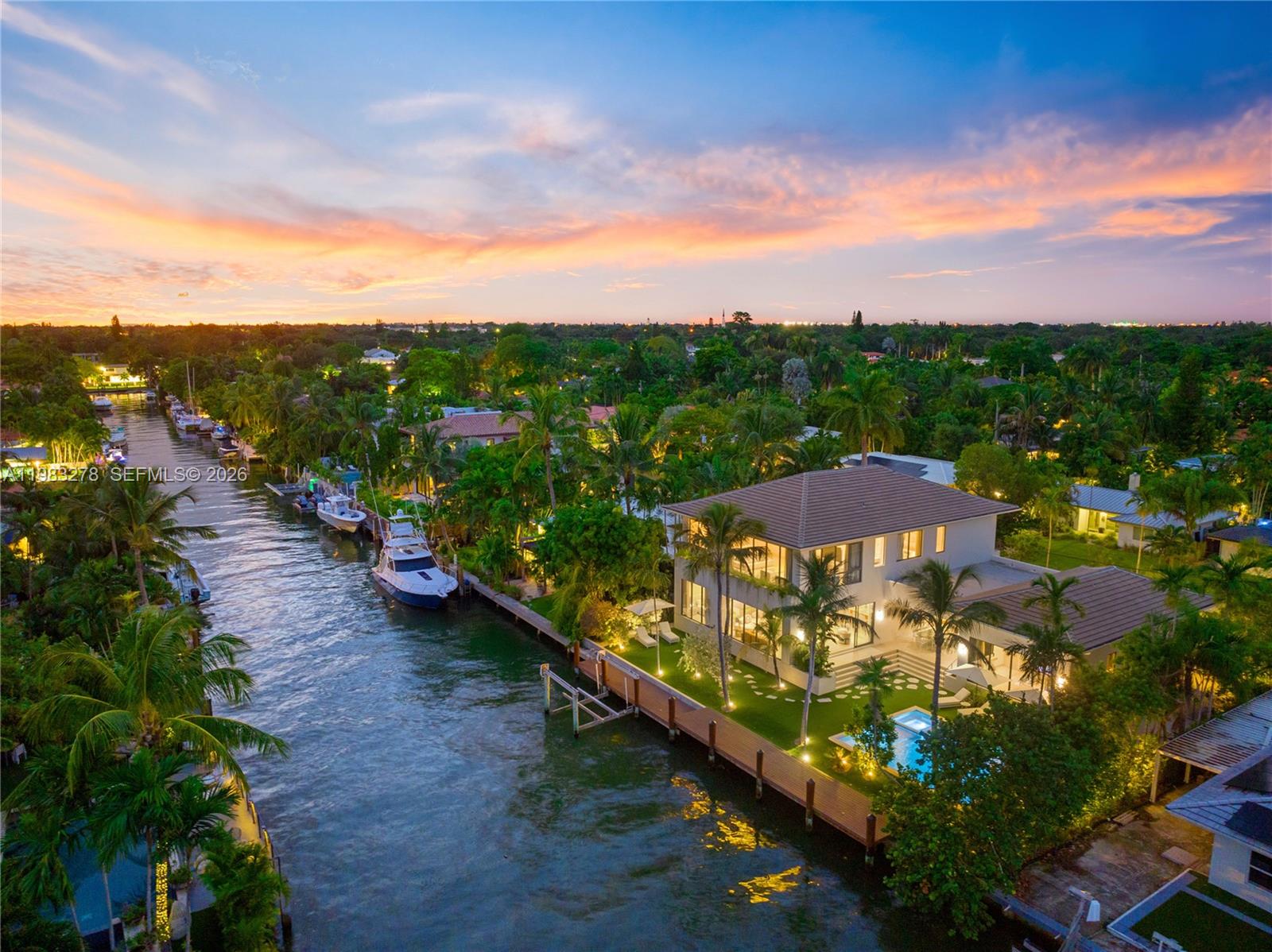 An aerial view shows a waterfront house with a pool, dock, and boats at sunset — 1200 NE 87th St, Miami FL 33138, MIAMI, FL