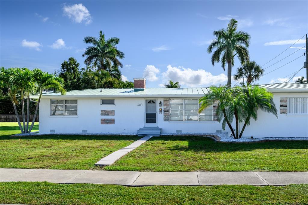 A white single-story house with a metal roof and palm trees in the front yard — 330 HARVEY STREET, PUNTA GORDA, FL