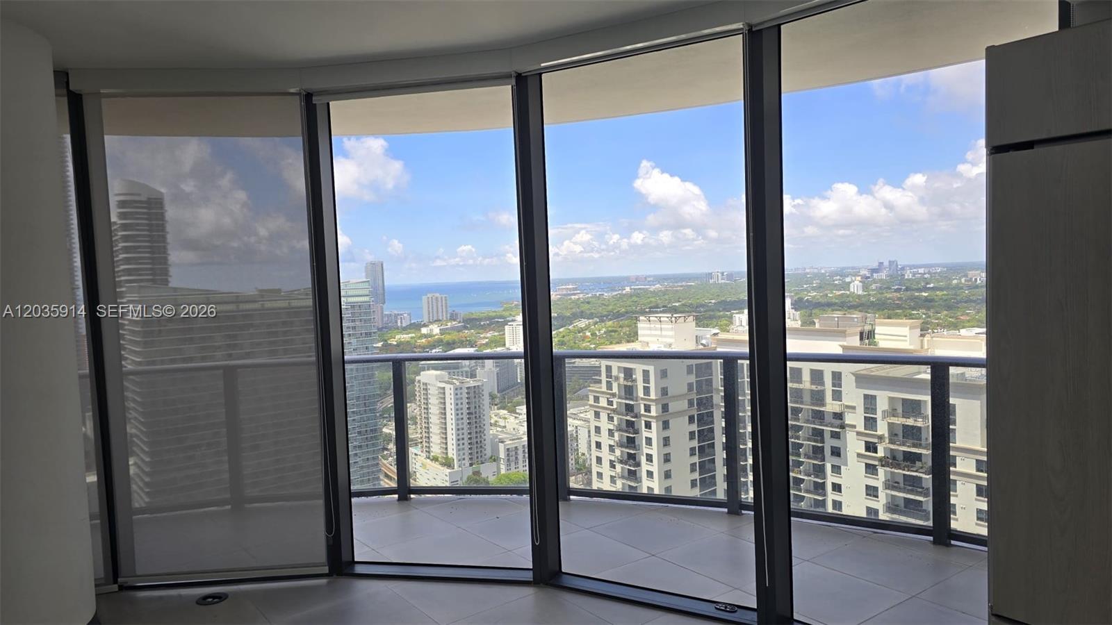 A room with floor-to-ceiling windows overlooks a balcony and a cityscape with water views — 45 SW 9th St # 3906, Miami FL 33130, MIAMI, FL