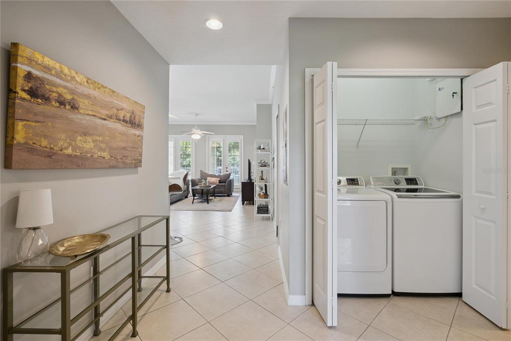 A hallway with a glass console table leads to a living area and laundry closet — 844 BLUE SAGE STREET UNIT 101, CELEBRATION, FL