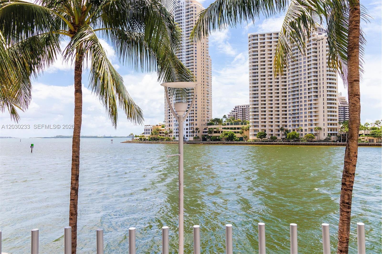 A view of a bay with tall residential buildings and palm trees in the foreground — 335 S BISCAYNE BLVD # 2908, Miami FL 33131, MIAMI, FL