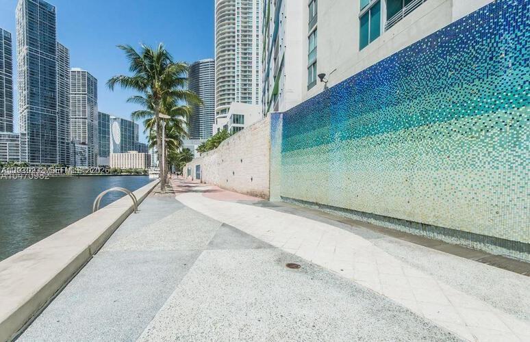 A paved waterfront walkway runs alongside a tall wall covered in blue mosaic tiles — 335 S BISCAYNE BLVD # 2908, Miami FL 33131, MIAMI, FL