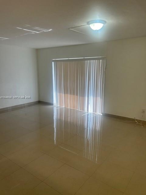 An empty room features light-colored tile flooring, white walls, and vertical blinds over a sliding door — 10395 N Kendall Dr # V4, Miami FL 33176, MIAMI, FL