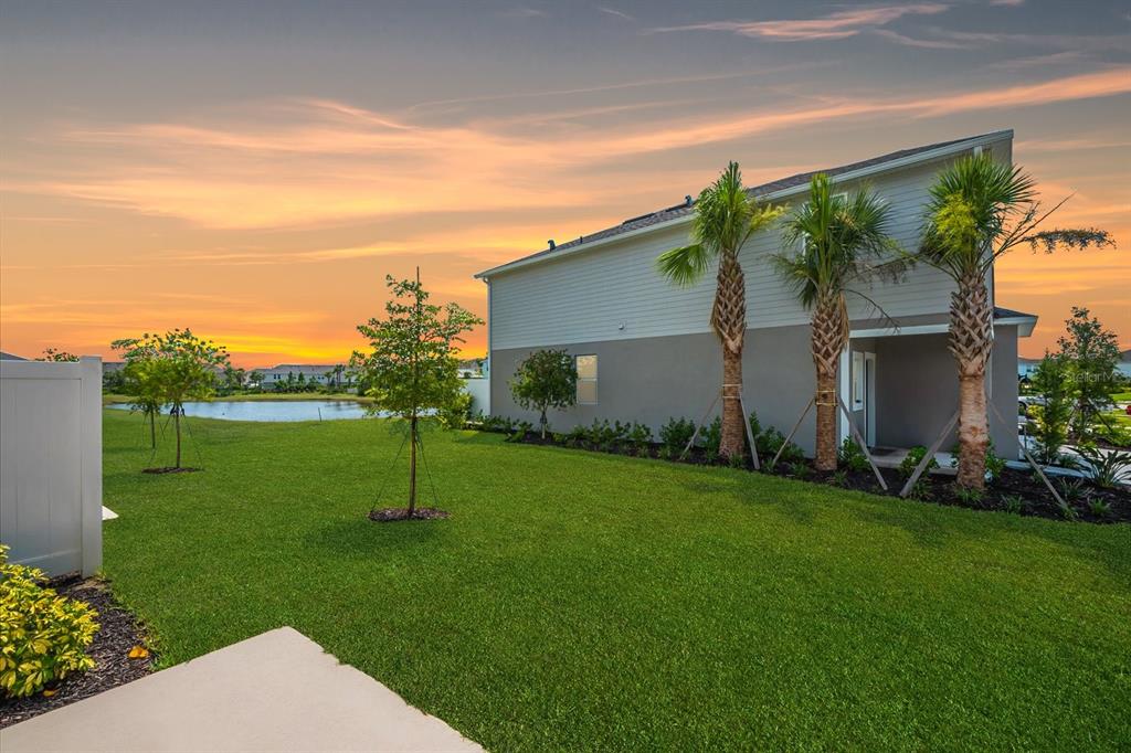 A side view of a two-story house with palm trees, a lawn, and a pond — 8701 WINTER BREEZE, SARASOTA, FL