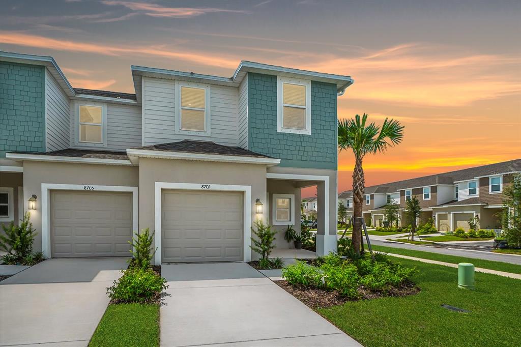 A two-story townhouse exterior features a beige stucco facade, teal shingle accents, and two garages — 8701 WINTER BREEZE, SARASOTA, FL