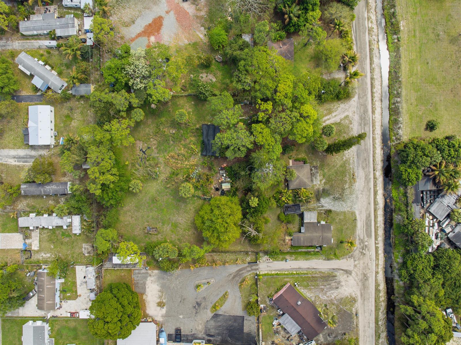 Aerial view of a residential property featuring several houses, dense trees, and a dirt road — 5133 Pine Grove Drive, West Palm Beach FL 33417, WEST PALM BEACH, FL