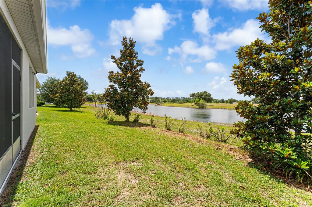 A grassy backyard overlooks a pond with several trees under a blue sky — 3300 SAGEBRUSH STREET, HARMONY, FL