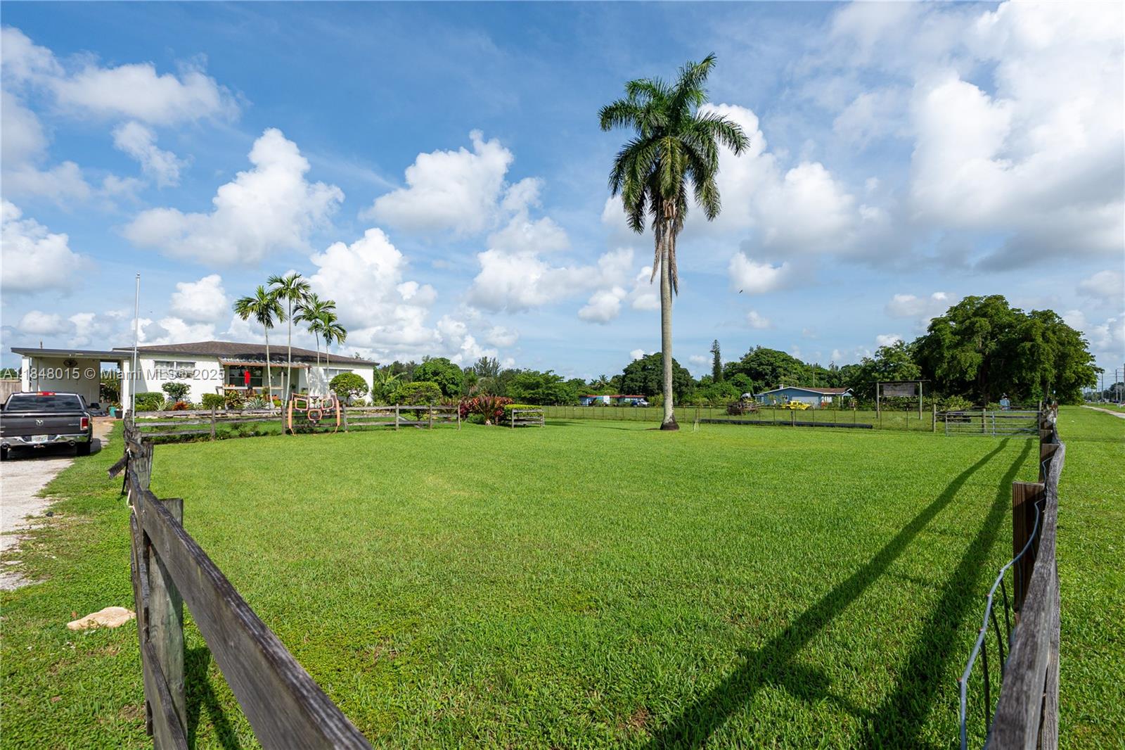 A large grassy yard is enclosed by a wooden fence with a house and palm trees — 1921 SW 112th Ave, Davie FL 33325, DAVIE, FL