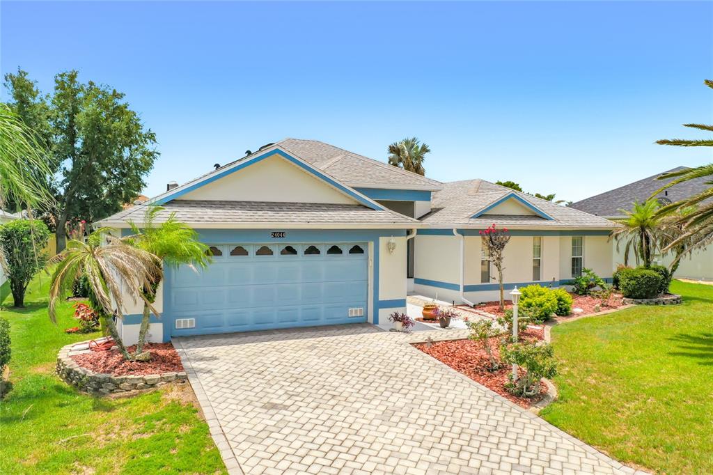 A single-story house with a blue garage door, light-colored stucco walls, and a paved driveway — 24044 PEEKSKILL STREET, LEESBURG, FL