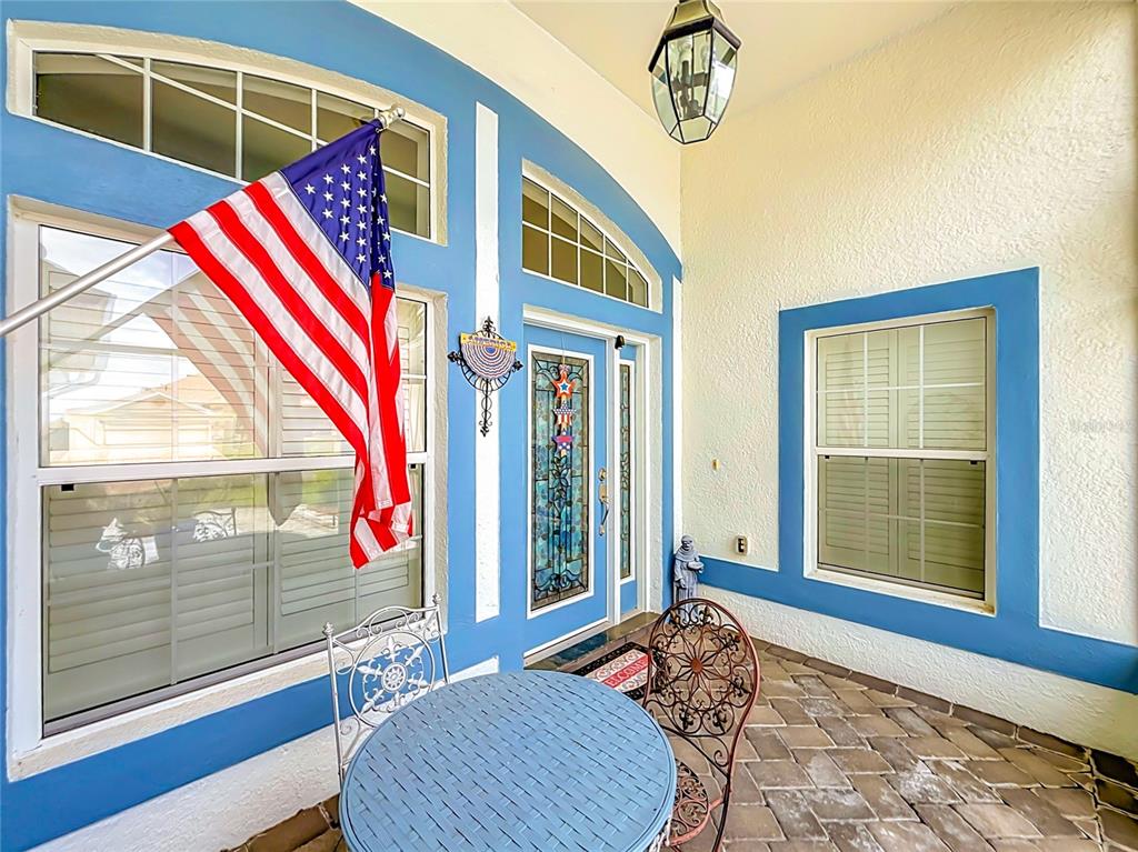 A covered front porch features a blue-trimmed entryway, an American flag, and patio furniture — 24044 PEEKSKILL STREET, LEESBURG, FL