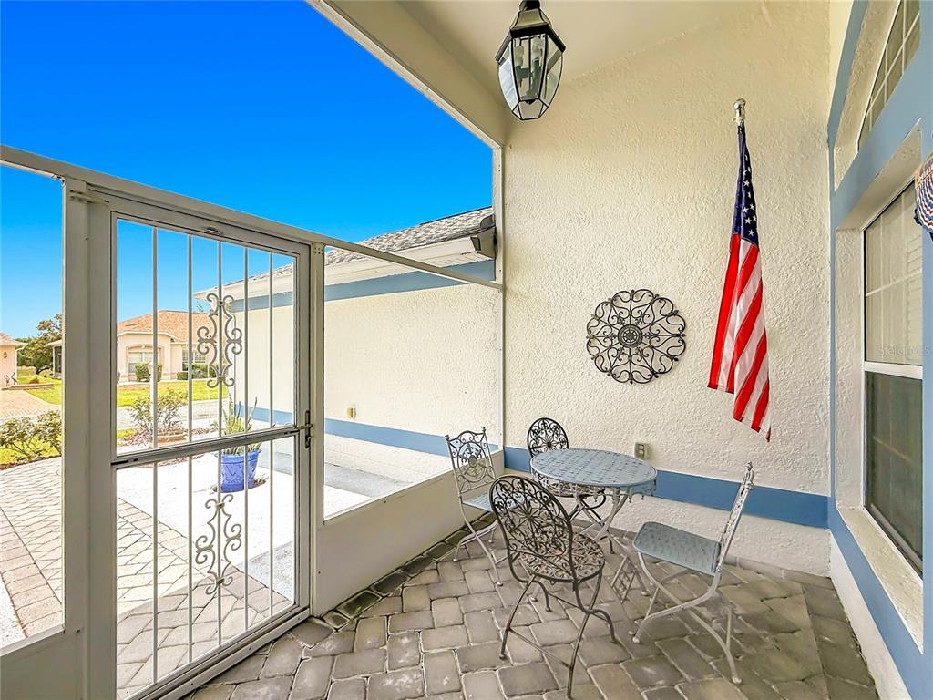 A screened-in patio features a small bistro set, a wall-mounted American flag, and pavers — 24044 PEEKSKILL STREET, LEESBURG, FL