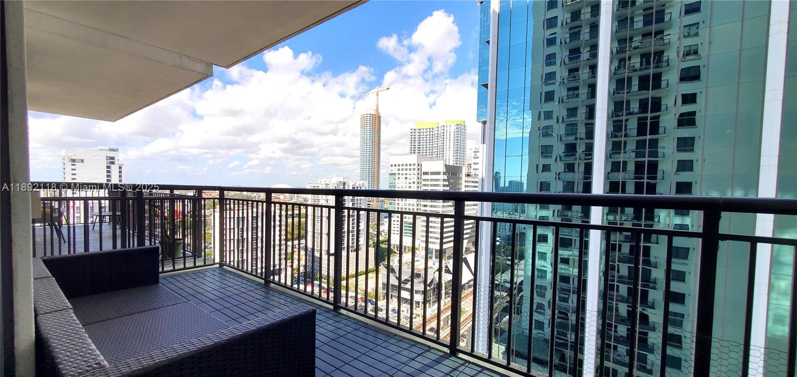 A high-rise balcony features dark wicker furniture and a view of surrounding city buildings — 999 SW 1st Ave # 2115, Miami FL 33130, MIAMI, FL
