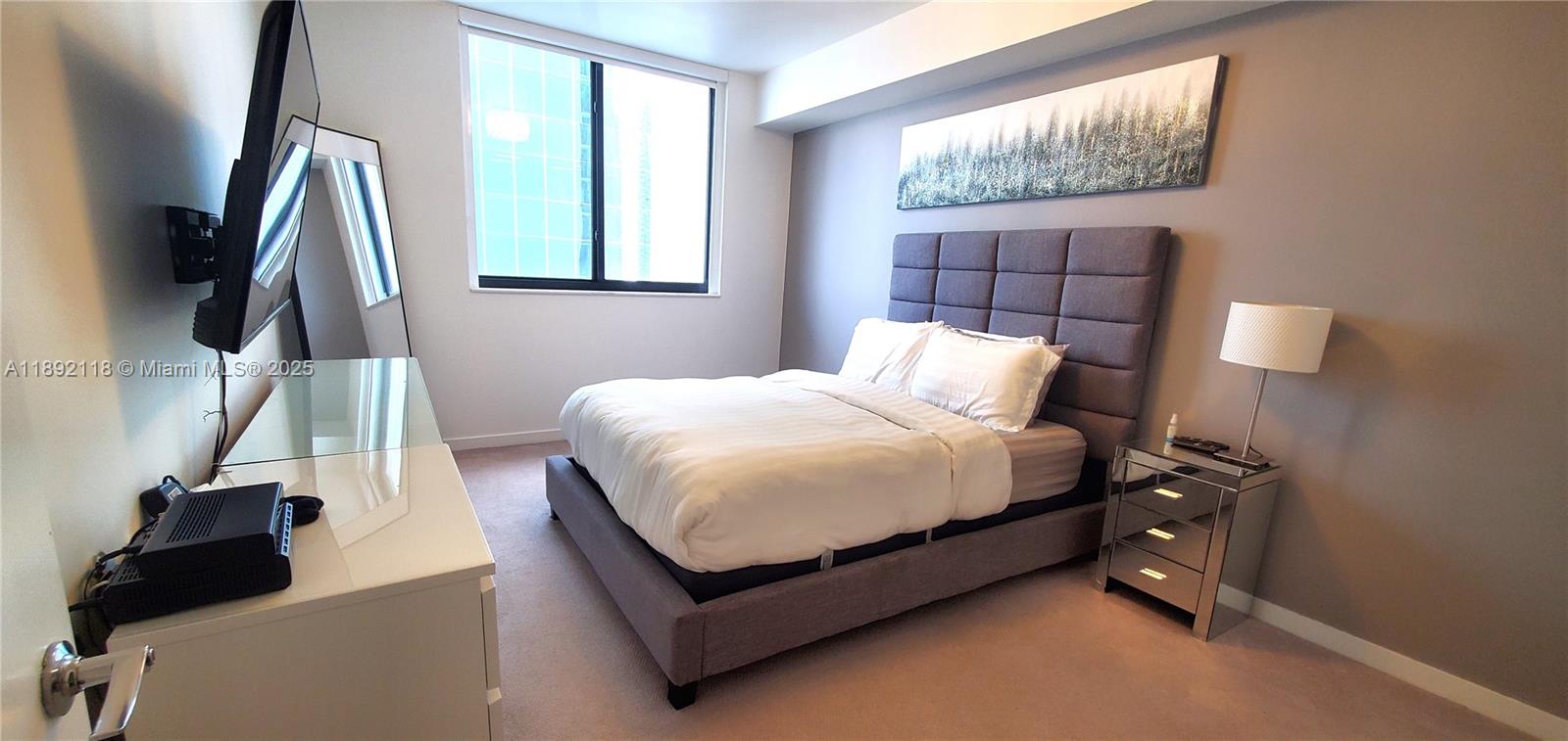 A bedroom features a gray upholstered bed, mirrored nightstand, and a wall-mounted television — 999 SW 1st Ave # 2115, Miami FL 33130, MIAMI, FL