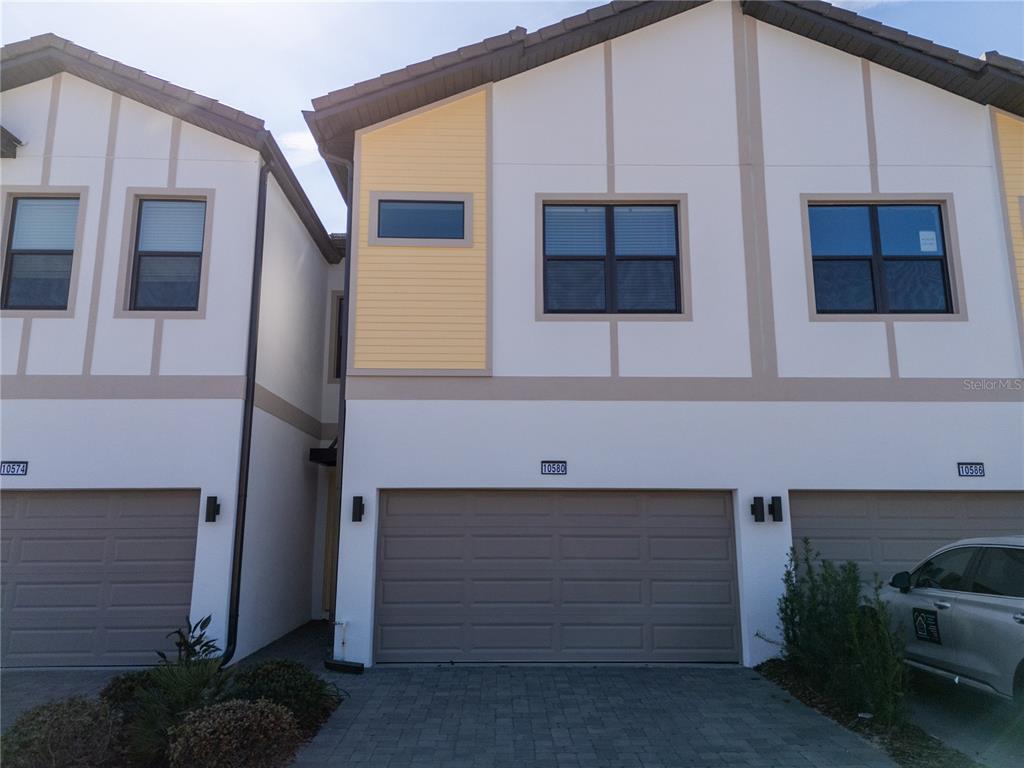 A row of three attached townhomes features beige garage doors and white stucco exteriors — 10580 EBB TIDE LANE, ORLANDO, FL