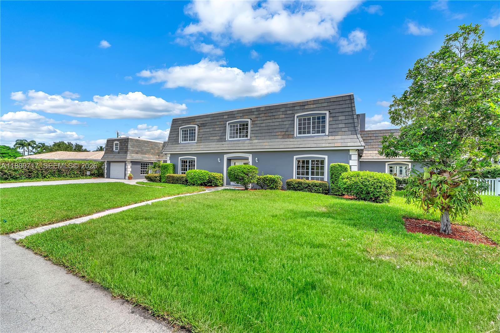 A two-story house with a mansard roof and gray exterior sits behind a green lawn — 4440 NE 23rd Ave, Lighthouse Point FL 33064, LIGHTHOUSE POINT, FL