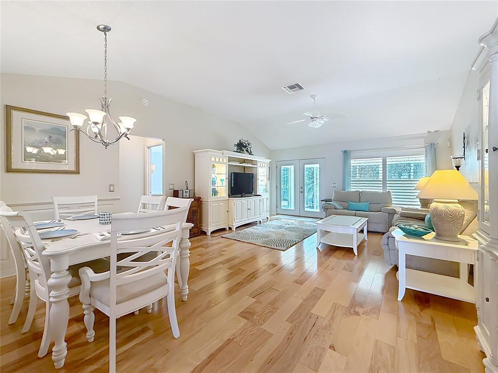 A bright open-concept living and dining area features hardwood floors, white furniture, and vaulted ceilings — 8641 SE 168TH KITTREDGE LOOP, THE VILLAGES, FL