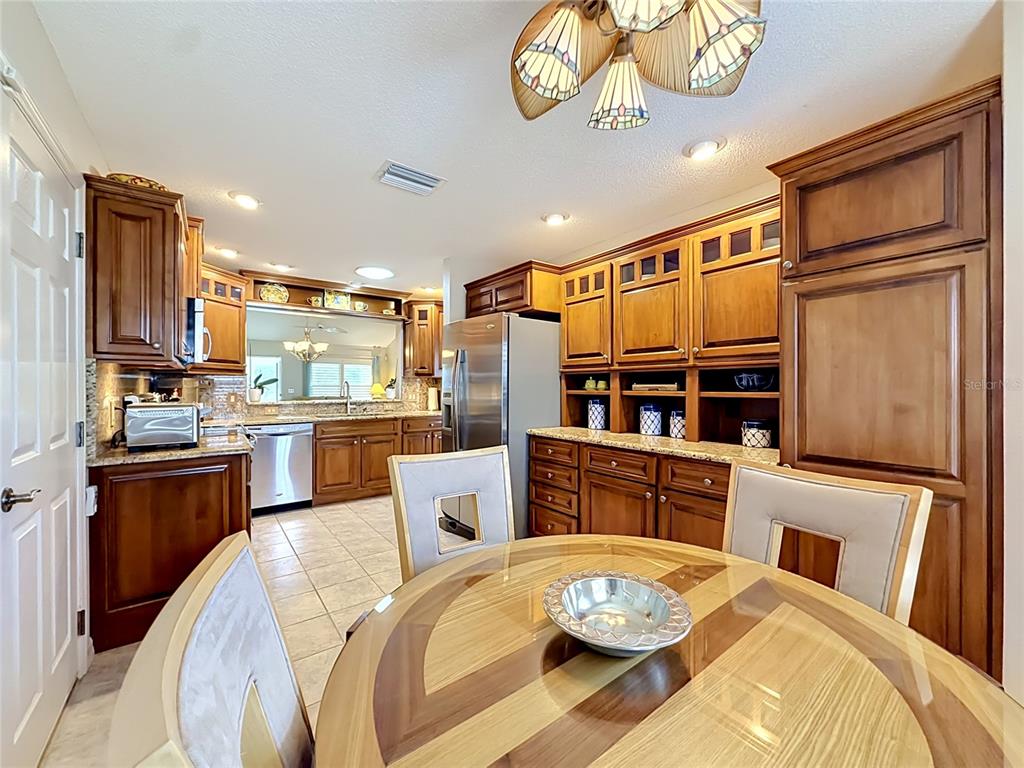 A kitchen with wood cabinets, granite countertops, stainless steel appliances, and a round dining table — 8641 SE 168TH KITTREDGE LOOP, THE VILLAGES, FL