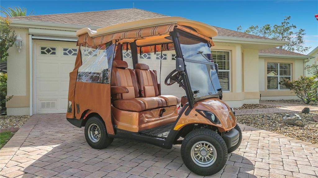 A bronze golf cart with a striped canopy sits on a paved driveway before a house — 8641 SE 168TH KITTREDGE LOOP, THE VILLAGES, FL