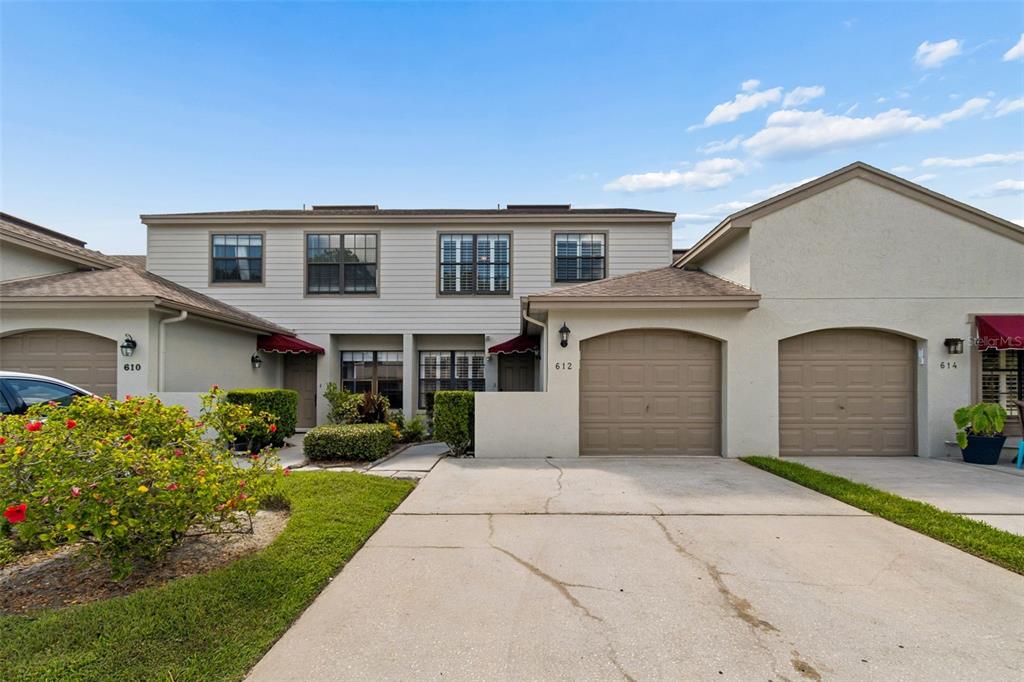 The exterior of a multi-unit townhouse complex features beige siding, tan garages, and concrete driveways — 612 QUAIL KEEP DRIVE, SAFETY HARBOR, FL