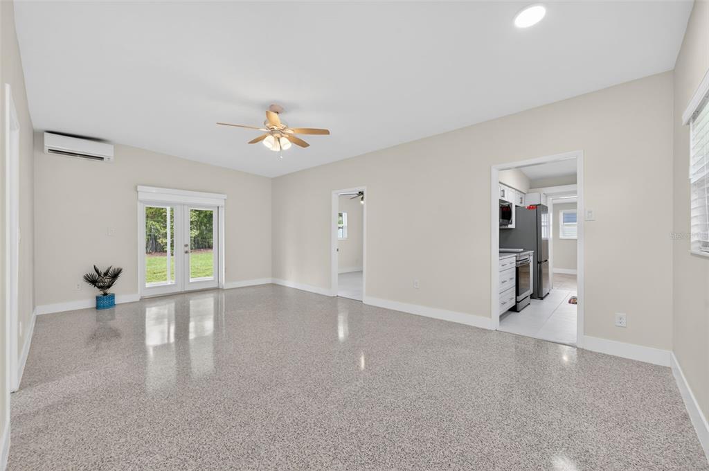 A spacious room with light-colored walls, a ceiling fan, and speckled flooring leads to a kitchen — 2974 CHANTILLY AVENUE, WINTER PARK, FL