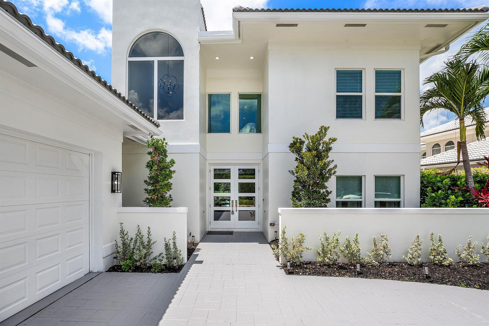 A white two-story house features a paved walkway leading to a double-door front entrance — 9701 Spray Drive, West Palm Beach FL 33411, WEST PALM BEACH, FL