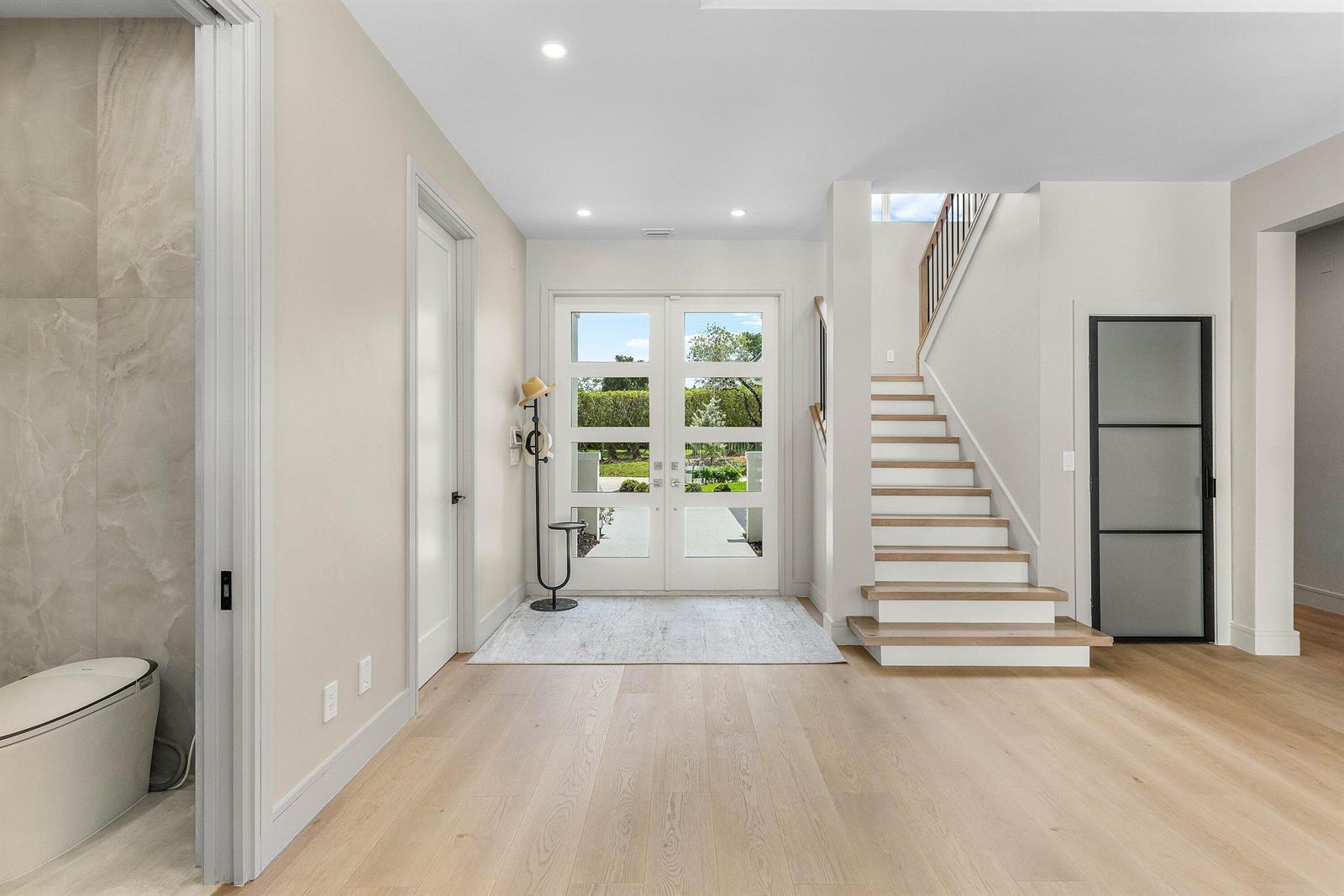 A bright entryway features light wood flooring, a staircase with wooden treads, and double glass doors — 9701 Spray Drive, West Palm Beach FL 33411, WEST PALM BEACH, FL