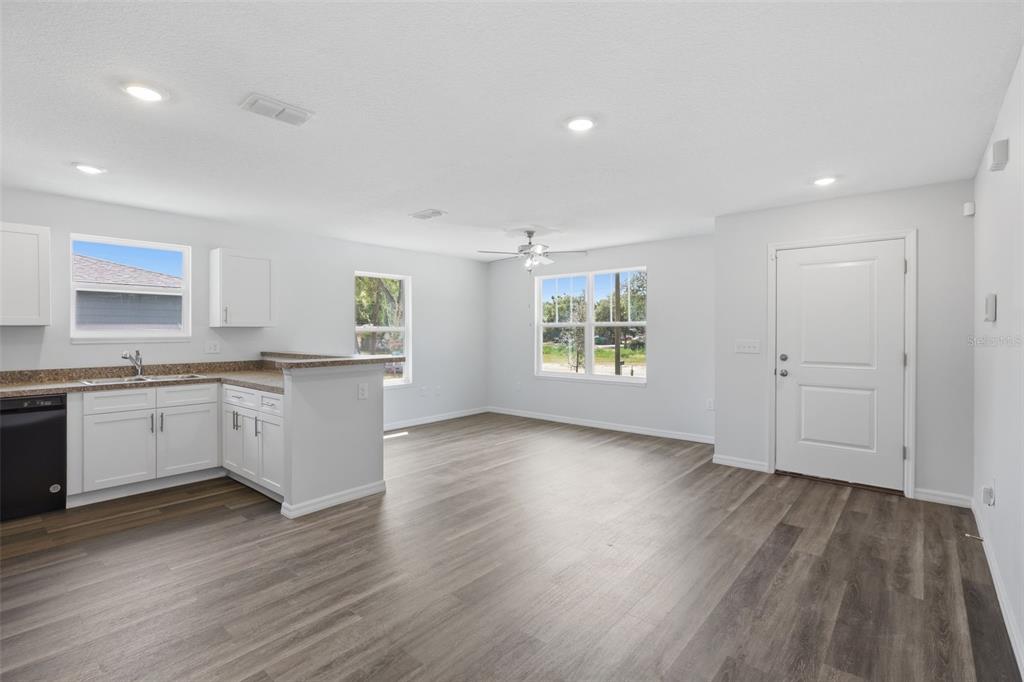 An open-concept kitchen and living area features white cabinets, grey flooring, and a front door — 3411 WARREN SAPP DRIVE, APOPKA, FL
