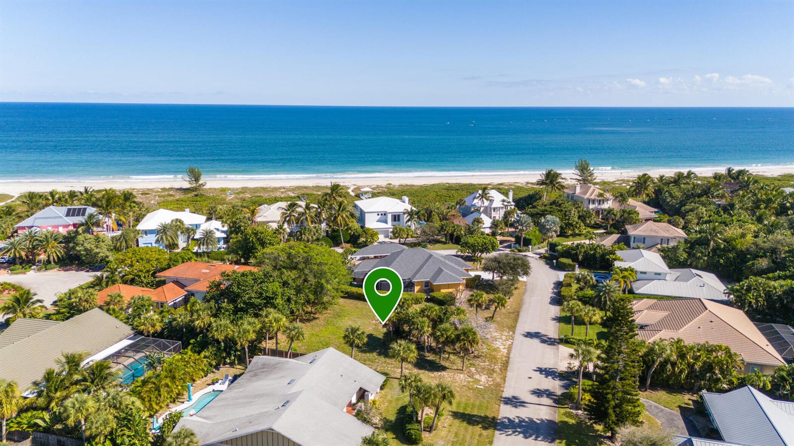 An aerial view shows a coastal neighborhood with houses, lush vegetation, and a sandy beach — 1370 White Heron Lane, Vero Beach FL 32963, VERO BEACH, FL