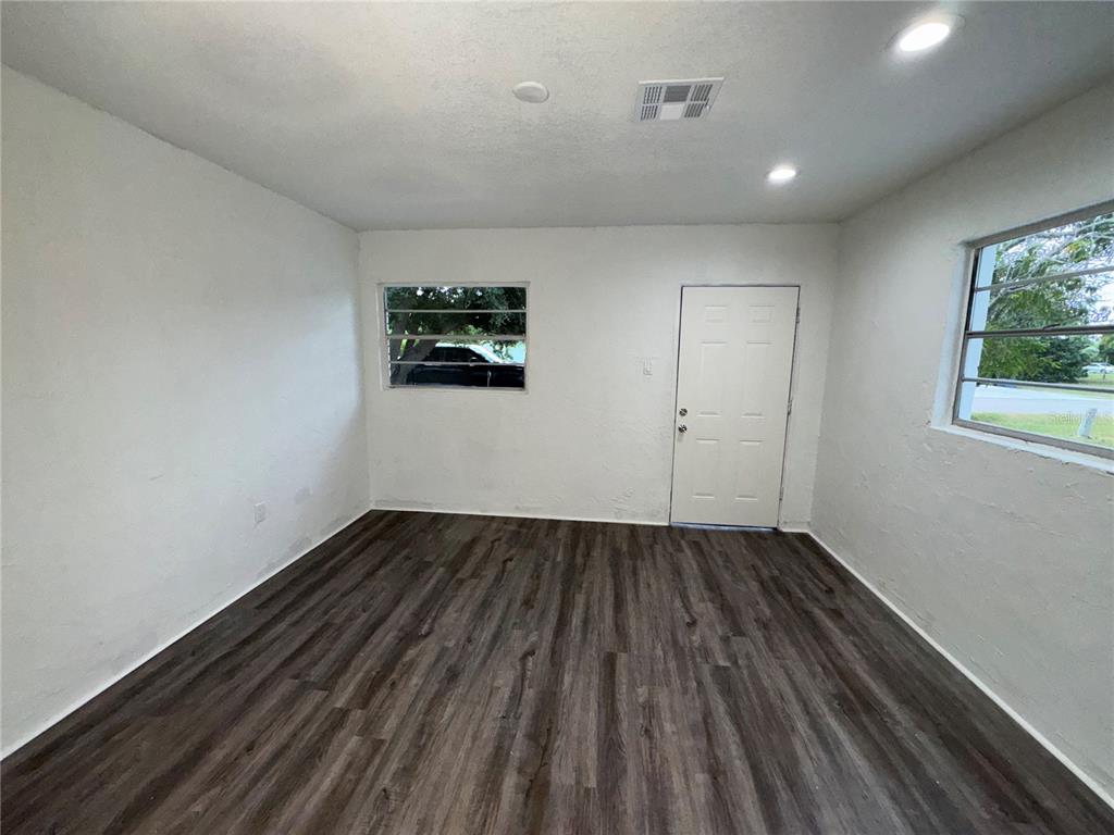 An empty room with white walls, dark wood-look flooring, two windows, and a white door — 521 SHOWALTER AVENUE, PUNTA GORDA, FL