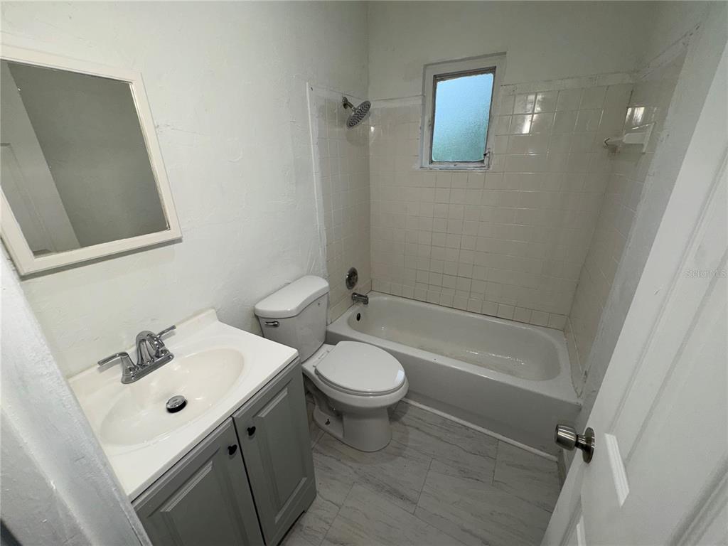 A small bathroom features a gray vanity, a white toilet, and a tiled shower-tub combo — 521 SHOWALTER AVENUE, PUNTA GORDA, FL