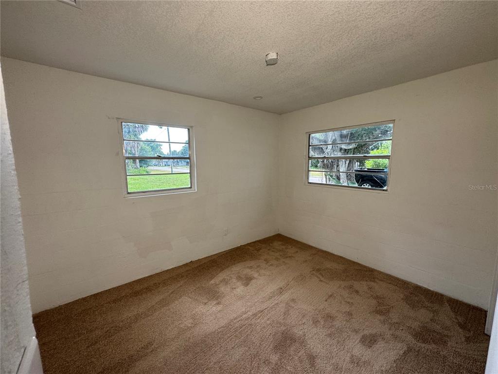 A bedroom with beige carpet, white walls, and two windows overlooking a yard — 521 SHOWALTER AVENUE, PUNTA GORDA, FL