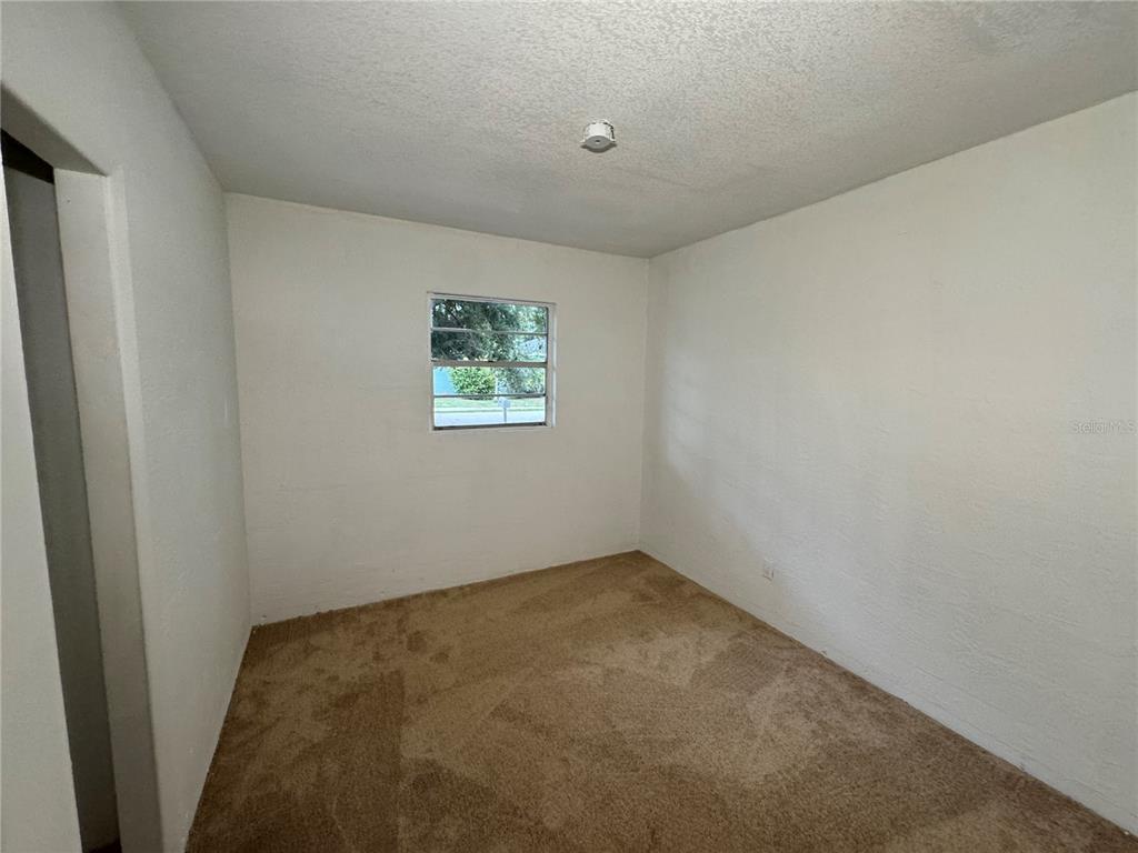 An empty bedroom features white walls, beige carpet, and a single window — 521 SHOWALTER AVENUE, PUNTA GORDA, FL